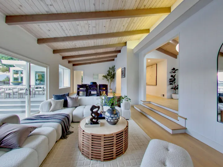 Remodeled living room with exposed ceiling beams and steps up to the dining area